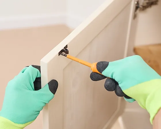 Mains effectuant un petit travail de bricolage avec tournevis sur une porte d'armoire