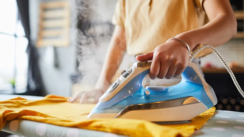 Repassage de linge à domicile, fer à vapeur sur tissu jaune